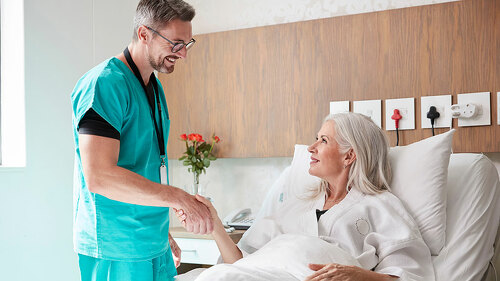 Surgeon Visiting And Shaking Hands With Mature Female Patient In Hospital Bed