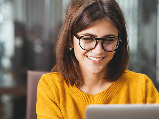 Portrait of happy business woman wearing glasses at workplace in office. Young handsome female worker using modern laptop