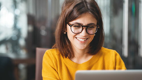 Portrait of happy business woman wearing glasses at workplace in office. Young handsome female worker using modern laptop