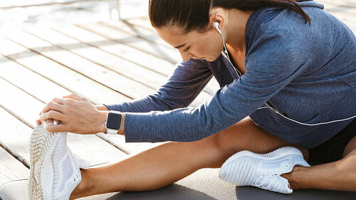 Fitness woman make stretching exercises at the beach outdoors listening music with earphones.