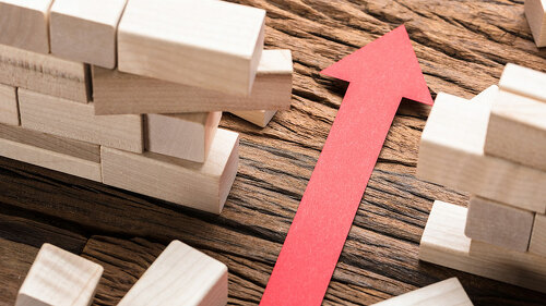 Red Paper Arrow Amidst Blocks On Wooden Table