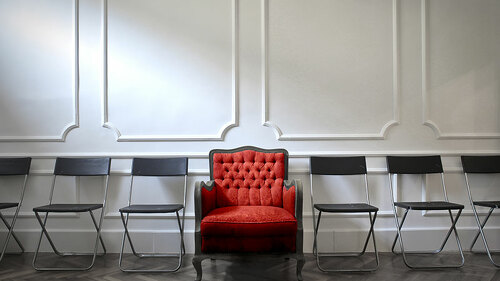 roter-sessel-zwischen-stuehlen-121400541-olly