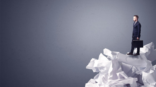 Anzugtraeger-steht-auf-Papierstapel-136555484-FO-ra2-studio