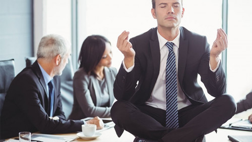 Anzugtraeger-meditiert-auf-Konferenztisch-105003101-FO-WavebreakmediaMicro