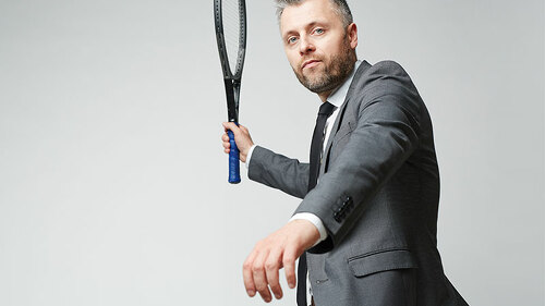 Anzugtraeger-schwingt-Tennisschlaeger-158815608-FO-pressmaster