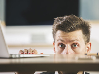 Anzugtraeger-versteckt-sich-unter-Tisch-162759425-FO-peshkova