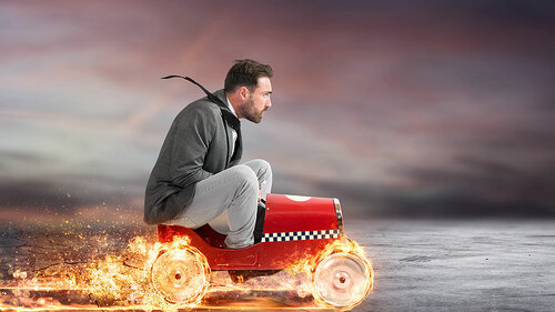 Anzugtraeger-in-Seifenkiste-mit-brennenden-Reifen-192886112-FO-alphaspirit